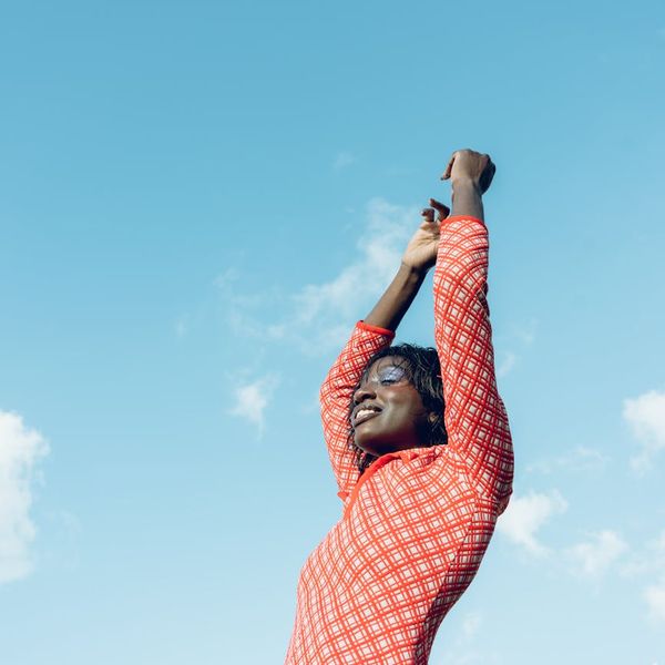 Person smiling and stretching outdoors under a clear blue sky.